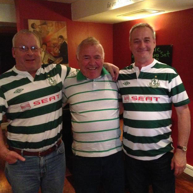 Three Shamrock Rovers fans smiling and celebrating together in a pub.
