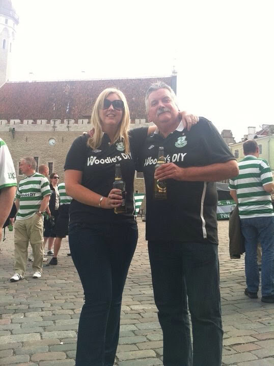 Shamrock Rovers supporters at a match, holding drinks and wearing team merchandise, celebrating at t.