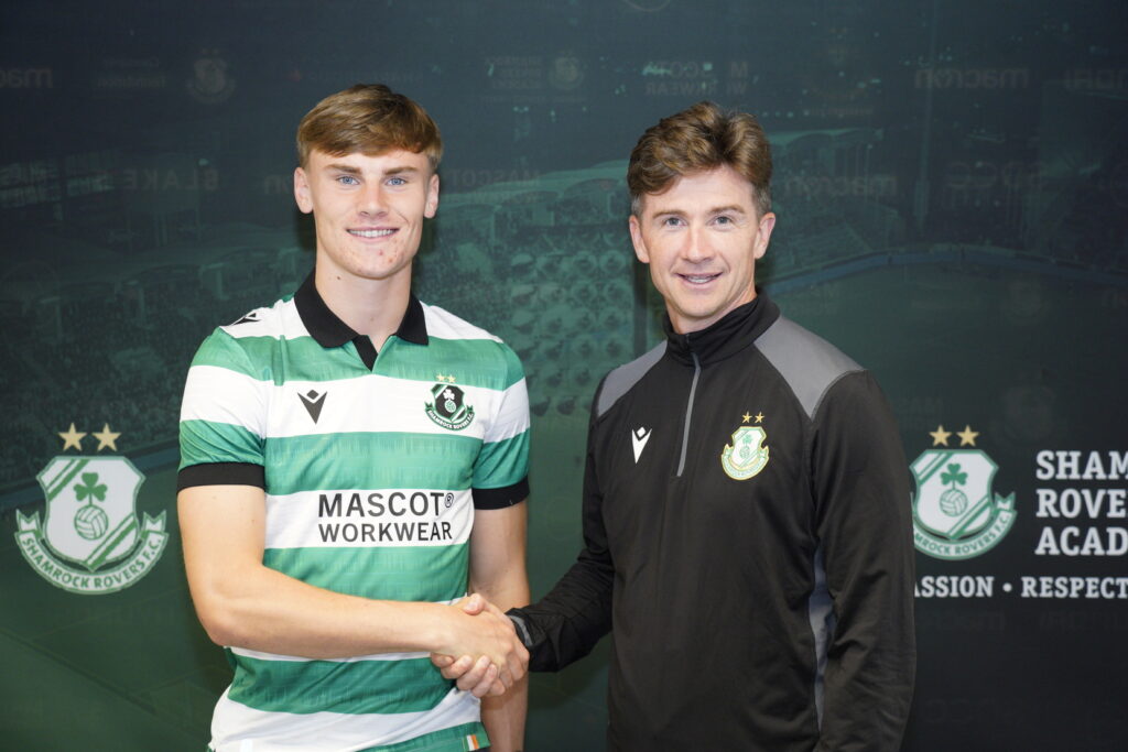 Shamrock Rovers player and coach shaking hands in front of club logo backdrop.
