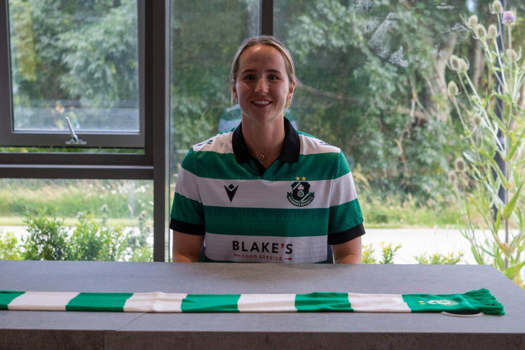 A female Shamrock Rovers player signing a jersey at a table.