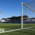 Empty football stadium with goalpost and League of Ireland logo.
